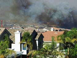 Smoke from an approaching wildfire can be seen hanging over a housing development in Southern California. By StacieStauffSmith Photos/Shutterstock.com